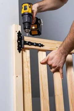 Hands Using Yellow and Black Cordless Drill on Wooden Gate Hinge Stock Photos