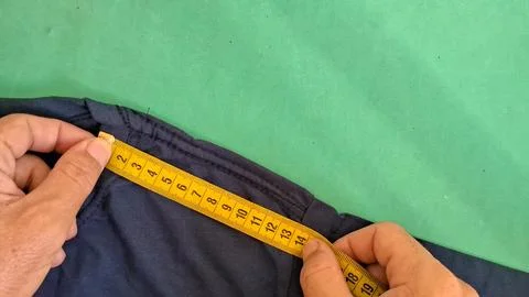 Hands using yellow measuring tape on dark blue fabric garment Stock Photos
