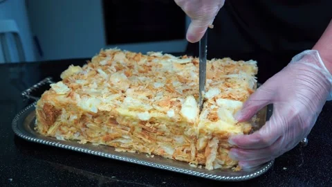 Hands in vinyl gloves cut knife layer cream puff cake Napoleon sprinkled crumbs Stock Footage 164669341