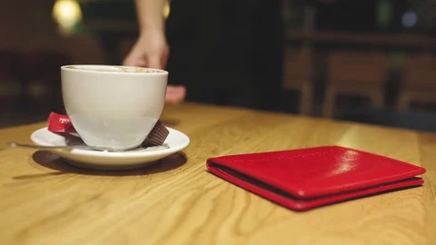 Hands of waiter taking away red leather bill or check folder and empty cup Stock Footage 123344882
