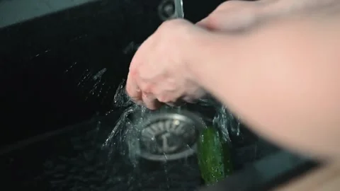 Hands wash a green vegetable under running water in a kitchen sink. The process Stockbeeldmateriaal 338304102