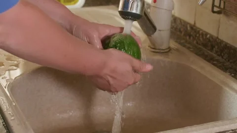 Hands washing avocado under running faucet, kitchen sink 库存影片 344728896