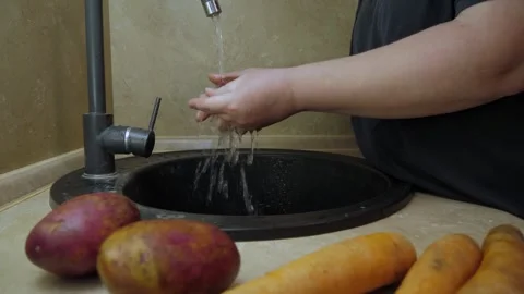 Hands washing potato beneath running faucet over kitchen sink Vidéo 342362025