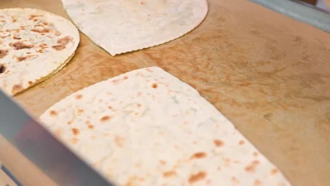Hands wearing black gloves work with flatbreads on a cooking surface in a Stock Footage 345885364