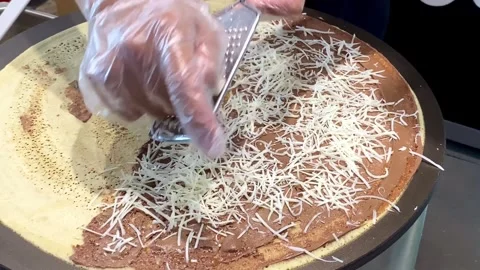 Hands wearing plastic gloves spread the batter on a hot crepe pan with choc.. Stock Footage 293646454