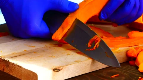 Hands wearing rubber gloves slice the pumpkin on a board. Stock Footage 153232130