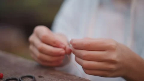 Hands weave thread. Quiet scene with hands knotting thread on outdoor bench Stock Footage 346387803