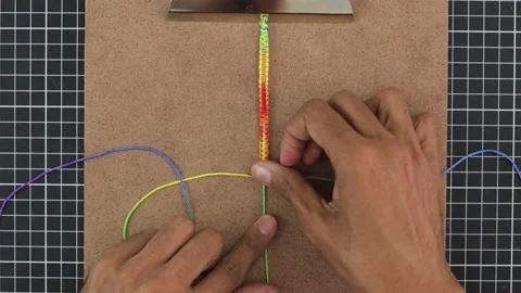 Hands weaving rainbow-patterned macrame bracelet, with colorful threads, Stock Footage 267059909