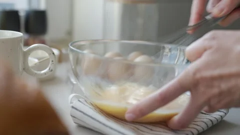 Hands whisk eggs in bowl on kitchen counter, with mug and extra eggs nearby Vídeo Stock 340151187