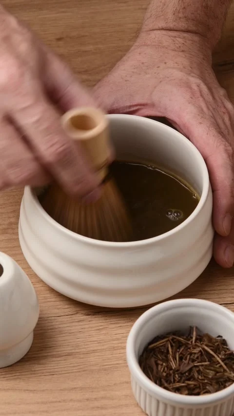 Hands whisk roasted hojicha powder with bamboo chasen in ceramic bowl during Video stock 340874580