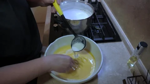 Hands whisk yellow batter while ladle pours milk Vídeos de archivo 342361756