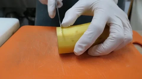 Hands in White Gloves Slicing Yellow Squash on Orange Cutting Board Stock Footage 345655875