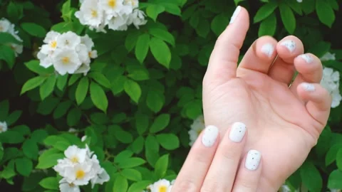 Hands with white speckled manicure on background of green plants and flowers. Stock Footage 277022746