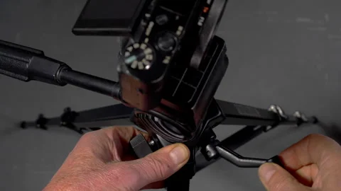 Hands winding a tripod handle to lower the camera shooting height. Stock Footage 242500272