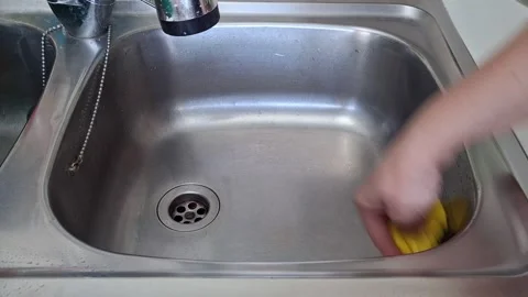 Hands wipe a kitchen sink using a yellow cloth in a home kitchen Stock Footage 343363775