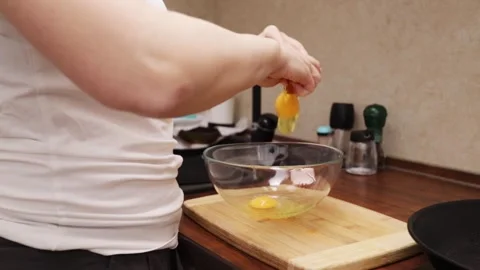 The hands of a woman cracking an eggshell and dropping it into a bowl Stock Footage 249384867