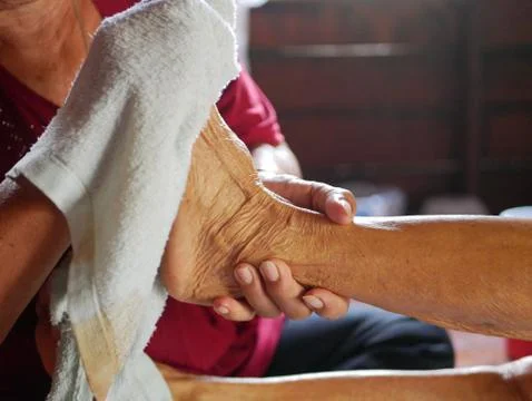 Hands of a woman holding an older person's feet, and giving a bed bath Stock Photos