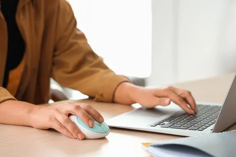 Hands of woman using computer mouse and laptop at table in office Stock Photos