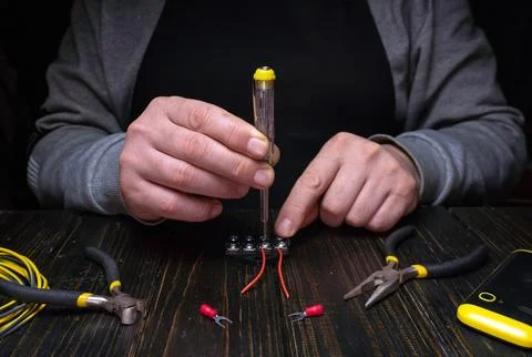 Hands work on electrical connections using tools in a dimly lit workspace Stock Photos