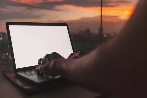 Hands work on the empty screen laptop with evening sunset city view. Stock-Fotos