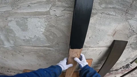 Hands in work gloves applying black paint with a brush to a wooden profile Stock Footage 336267779