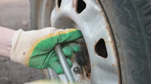 Hands work to remove a tire using a wrench and jack in an outdoor environment Stockbeeldmateriaal 337550609