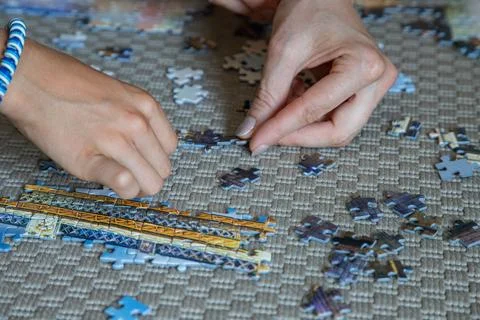Hands work together on a large jigsaw puzzle on a carpeted floor at home Stock Photos