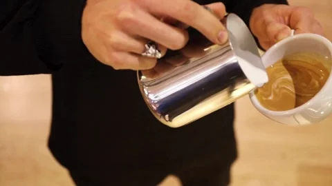 Hands of a worker making a cappuccino latte art in a cup at a coffee shop. 動画素材 334648332