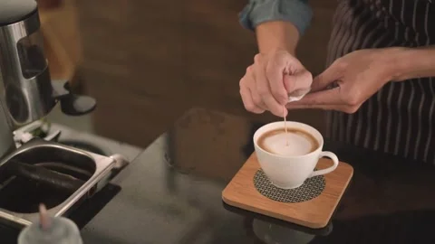 Hands of a worker making a cappuccino latte art in a cup at a coffee shop. 動画素材 334648349