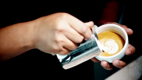 Hands of a worker making a cappuccino latte art in a cup at a coffee shop. 動画素材 334648368