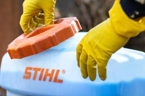 The hands of a worker in protective gloves open the lid of a tank with garden Stock Photos