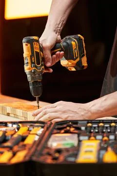 The hands of a worker screw a self-tapping screw into a wooden blank using an Foto stock