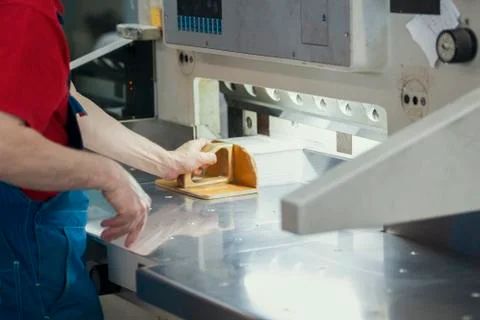 Hands of worker in typography puts the paper on cutter guillotine machine Stock Photos