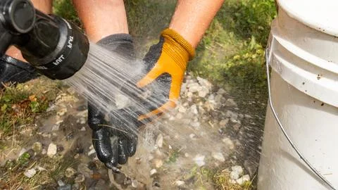 Hands of a worker using a pressure washer to clean gravel and stones, showcasing Stock Photos