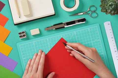 Hands working with colorful paper using a precision knife on a mint green cut Stock Photos