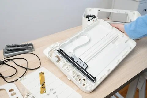 Hands working on a disassembled flatbed scanner laid out on a light wooden de Stock Photos
