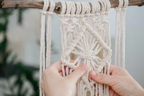 Hands working on a macrame piece suspended from a stick. Stock Photos