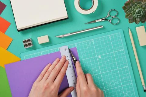 Hands working with violet paper using a paper knife on mint green cutting m.. Stock Photos