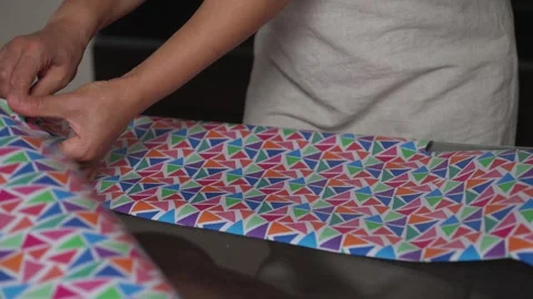 Hands Wrapping Colorful Geometric Pattern Paper in a Modern Interior Stock Footage 316838122