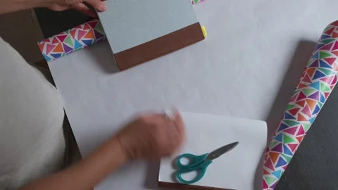 Hands Wrapping Gift with Colorful Geometric Paper and Scissors Stock Footage 316836247