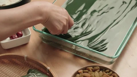 Hands Wrapping Green Leaf Rice Dumplings on Wooden Table Stockbeeldmateriaal 339069829