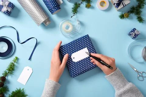 Hands write on a gift label. Around it are ribbon, scissors, tape, spruce t.. Stock Photos