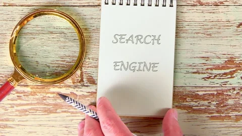Hands write or reveal the words Search Engine on a small spiral notepad resting Stock Footage 328072687