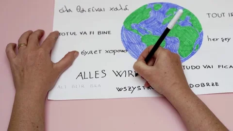 Hands writing all will be ok in many languages around colored earth Stock Footage 279437273