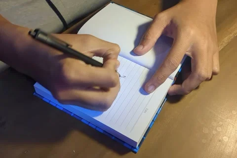 Hands writing with a black pen in a lined notebook Stock Footage 338146030