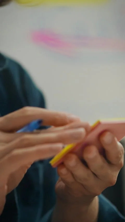 Hands writing notes on a sticky pad in a modern workspace Stock Footage 331592782