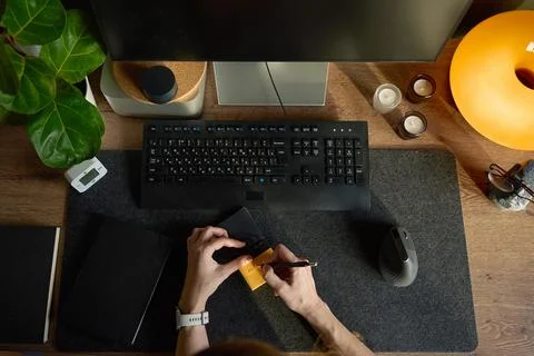 Hands writing on sticky note at desk with keyboard, monitor, mouse and note.. Foto stock