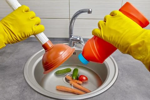 Hands in yellow rubber gloves hold a plunger and a pipe cleaner Stock Photos