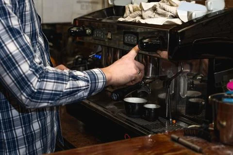 Hands of young bartender in uniform making espresso coffee on coffee machin.. Stock Photos