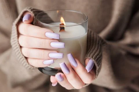 The hands of a young girl with a beautiful light purple manicure hold a candl Stock Photos